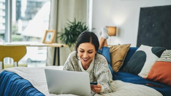 Shot of a young woman using a laptop and credit card on the bed at home