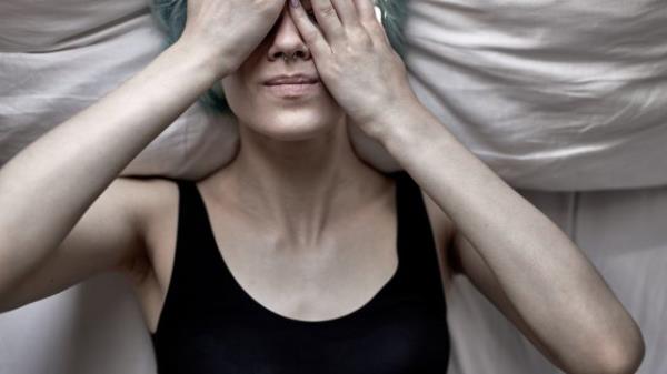 young woman lying down with her hands covering her face feeling unwell